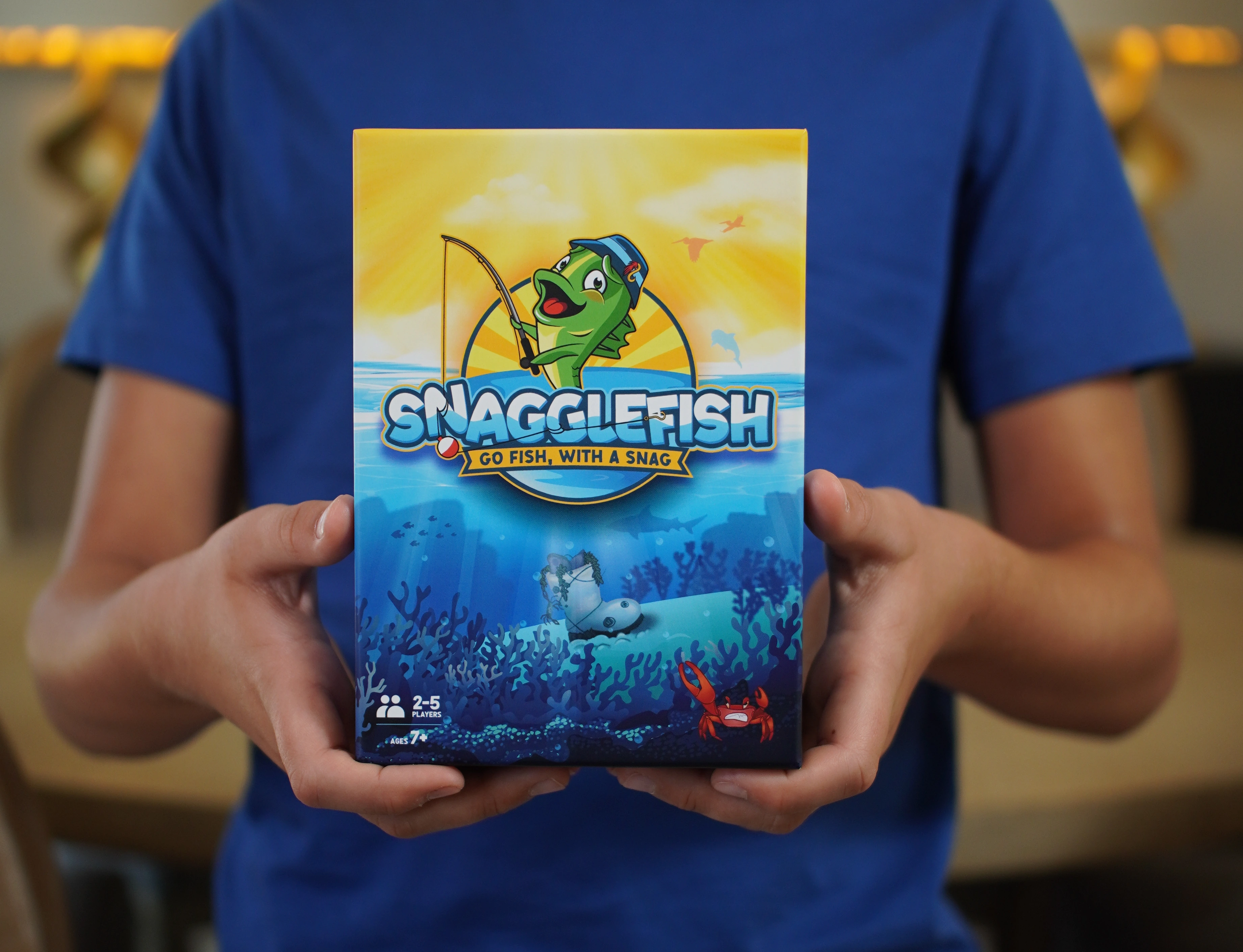 Blue-shirted young player holding the original Snagglefish box, cropped to show only hands and torso